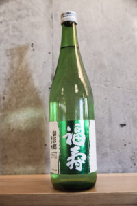 a bottle of Fukuju Junmai against a concrete wall