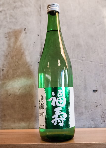 a bottle of Fukuju Junmai against a concrete wall