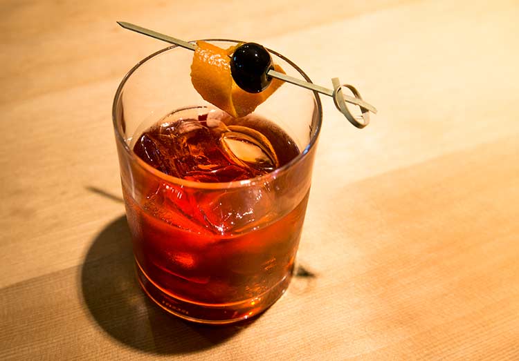 a red-colored cocktail with an orange and cherry garnish