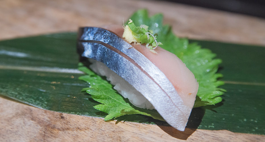 a piece of saba sushi topped with ginger and scallion