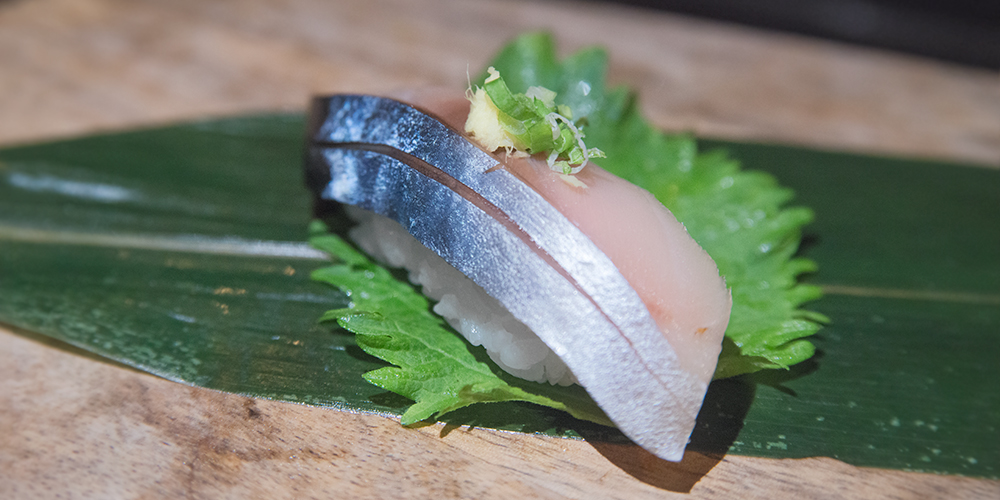 a piece of saba sushi topped with ginger and scallion