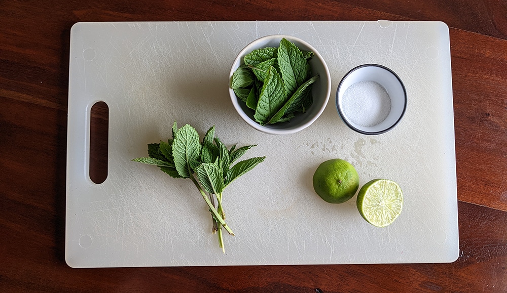 lime, mint leaves, mint tops, and sugar on a cutting board