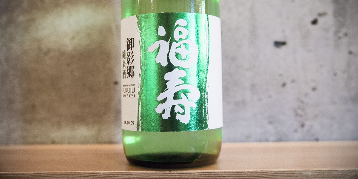 a green bottle of sake on a wood shelf