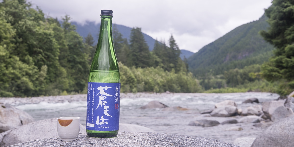 a blue and green bottle of sake next to a mountain river