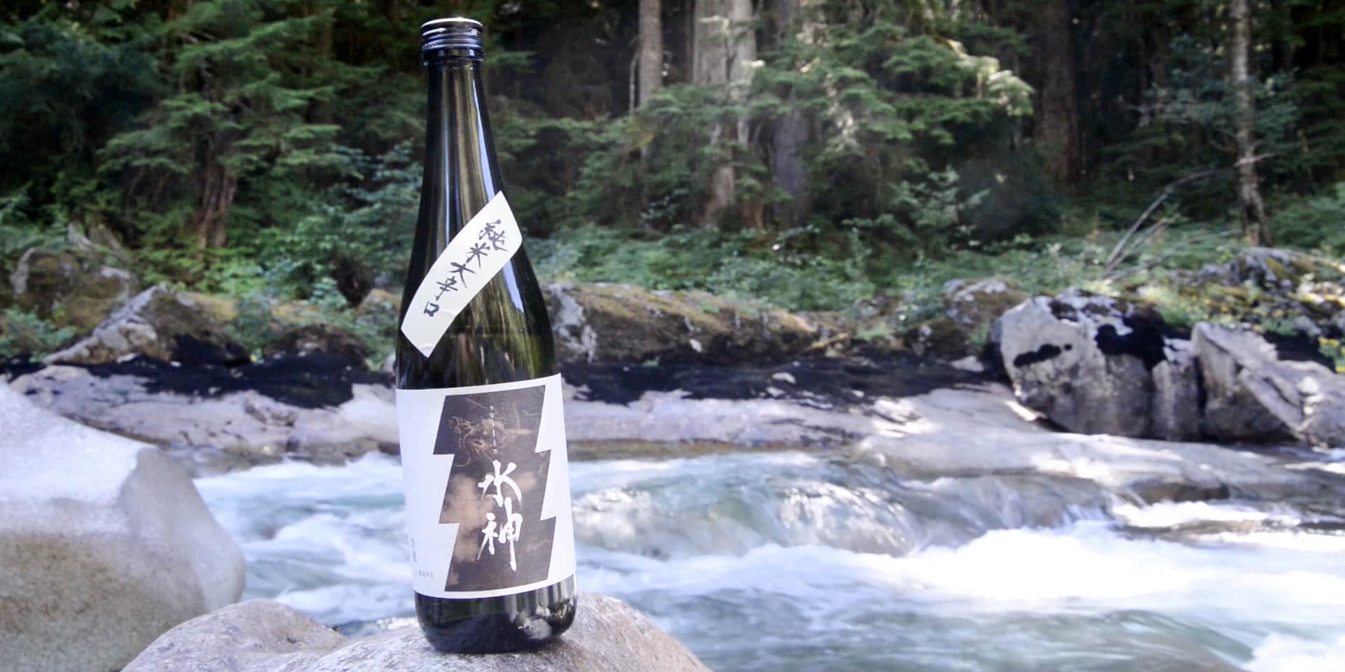 a bottle of sake next to a mountain stream